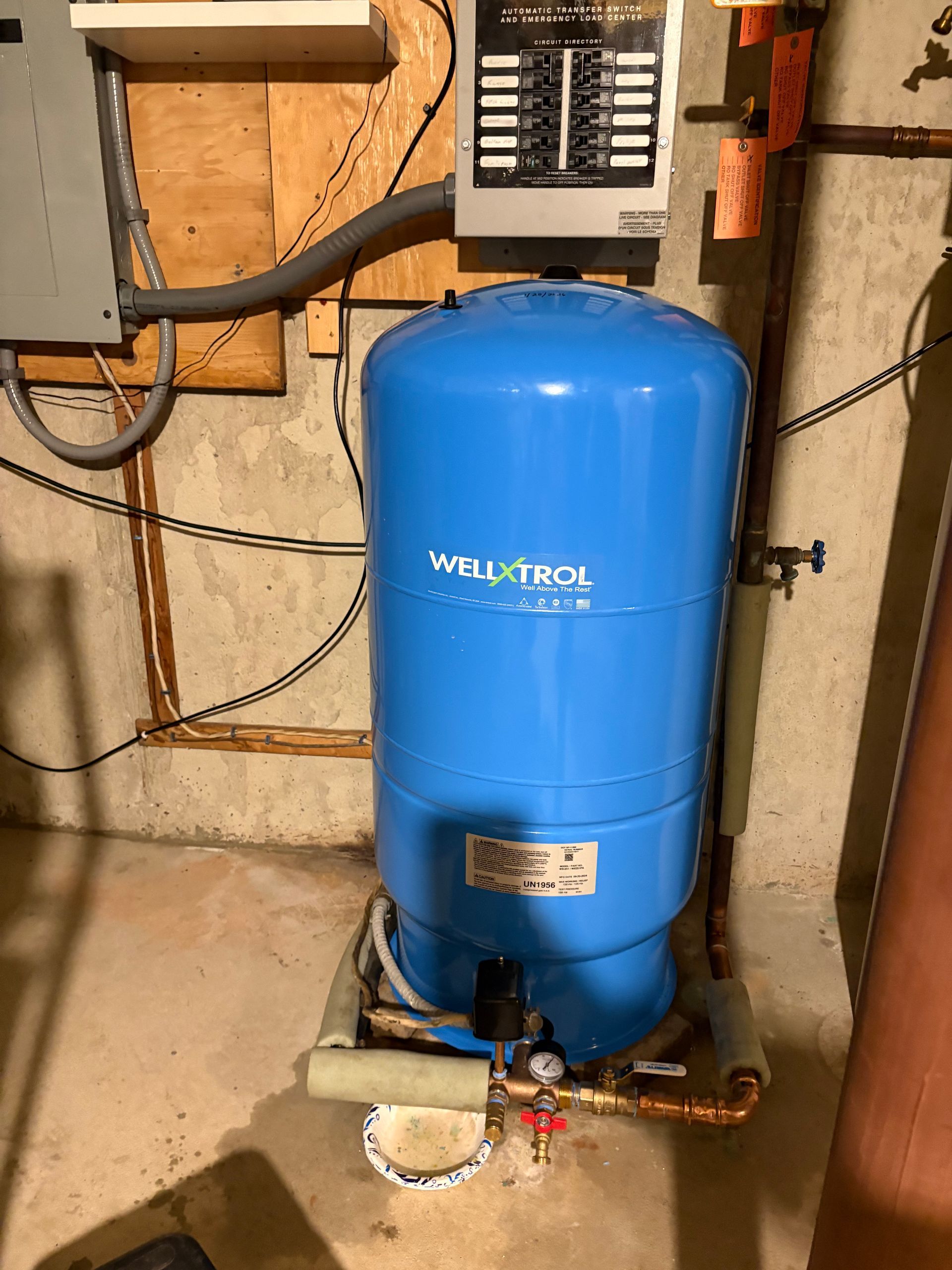 Blue well pressure tank with a control panel in a basement setting.