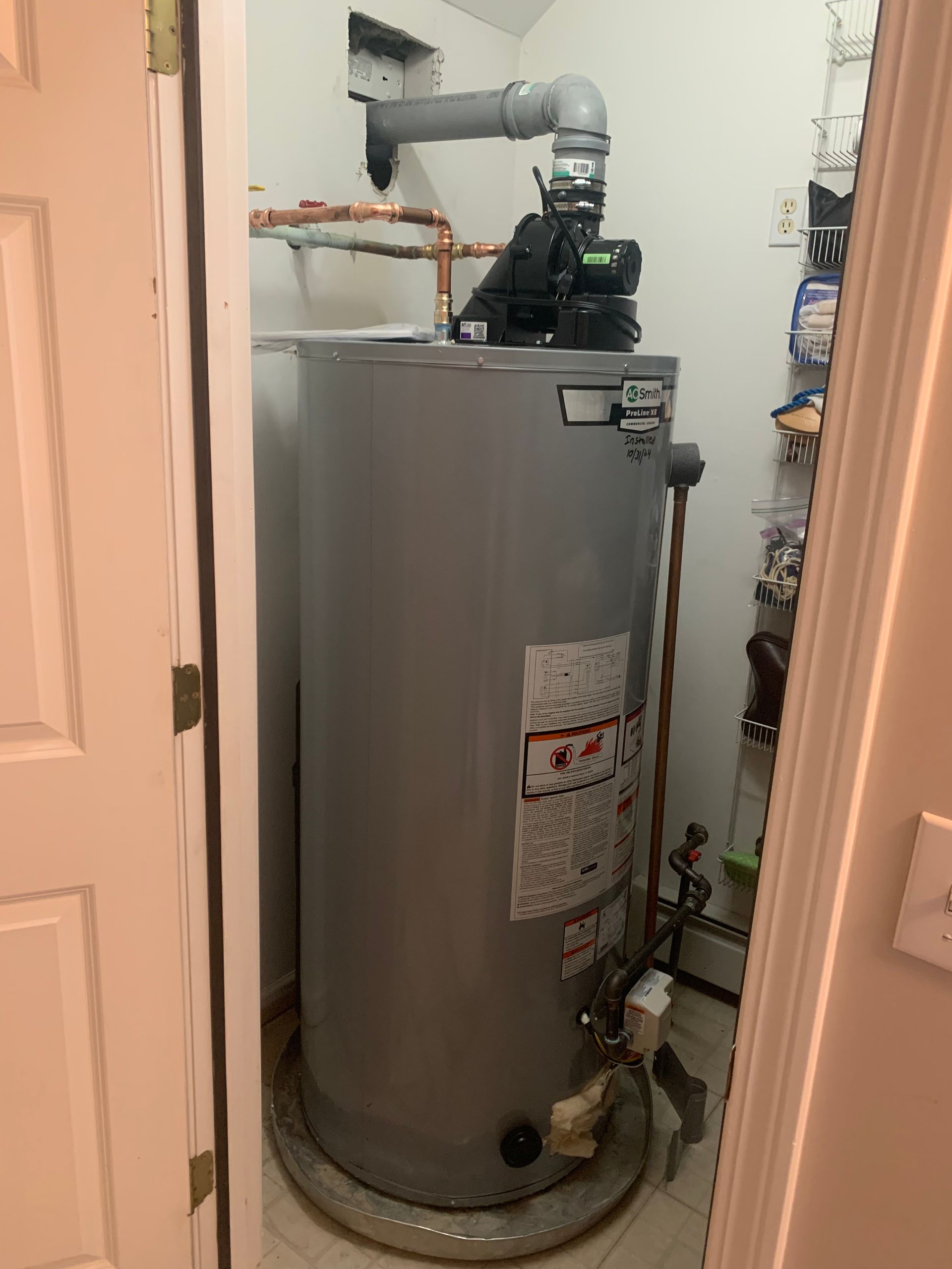 Water heater in a utility closet with copper pipes, a pump, and a vent pipe.