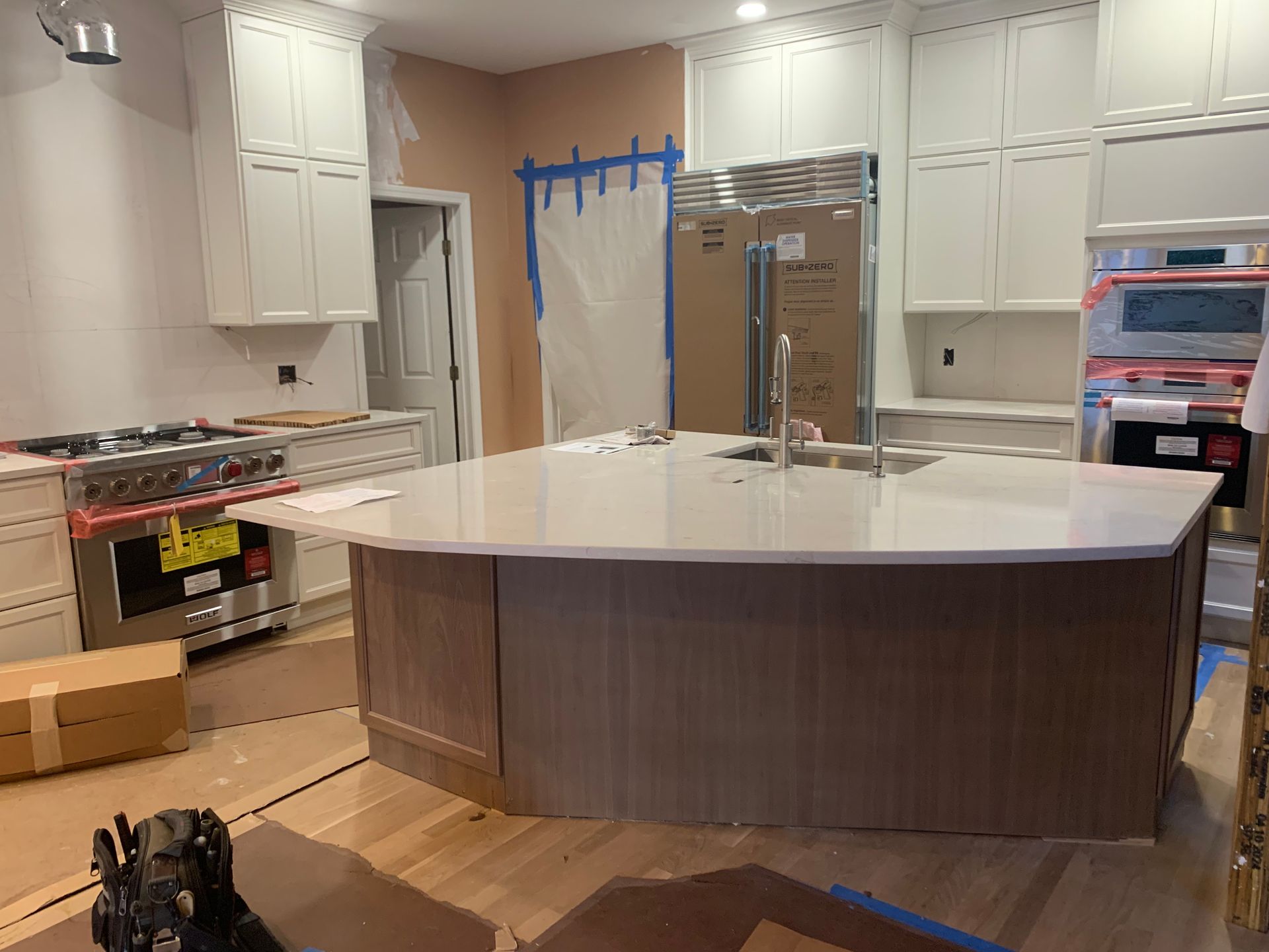 Kitchen under construction with island, cabinets, appliances, and cardboard boxes.