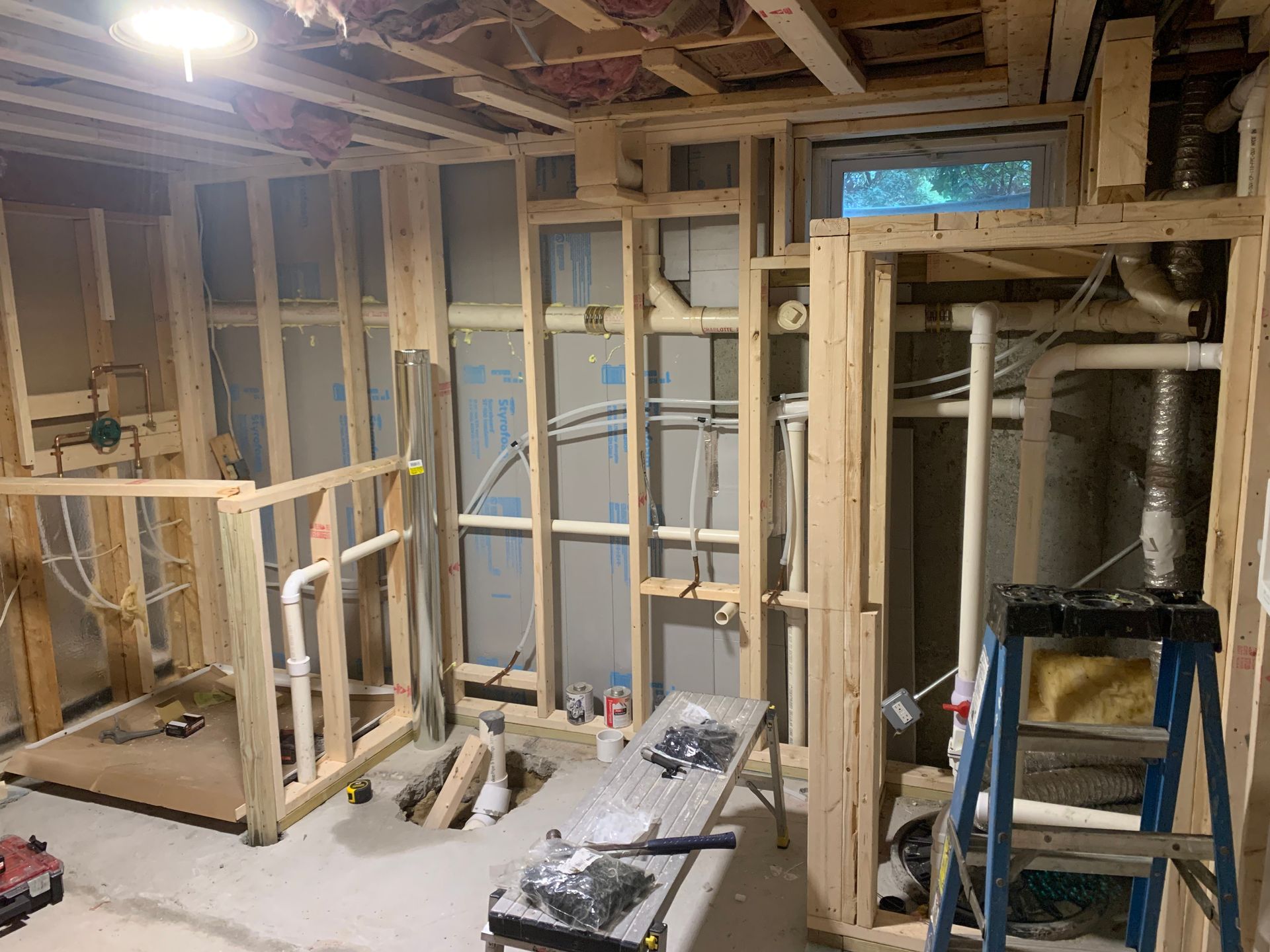 Basement room under construction: wood frame walls, pipes, wires, exposed studs, and a ladder.