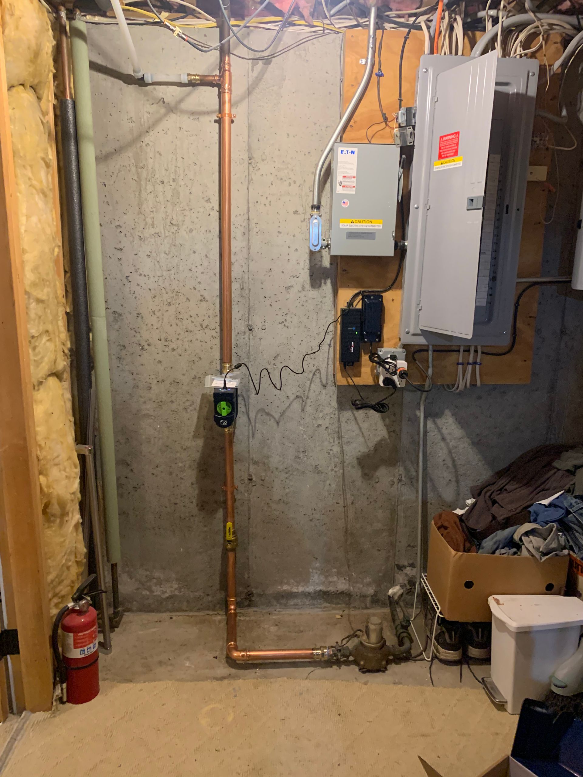 Basement with copper pipes, electrical panel, and fire extinguisher against a concrete wall.