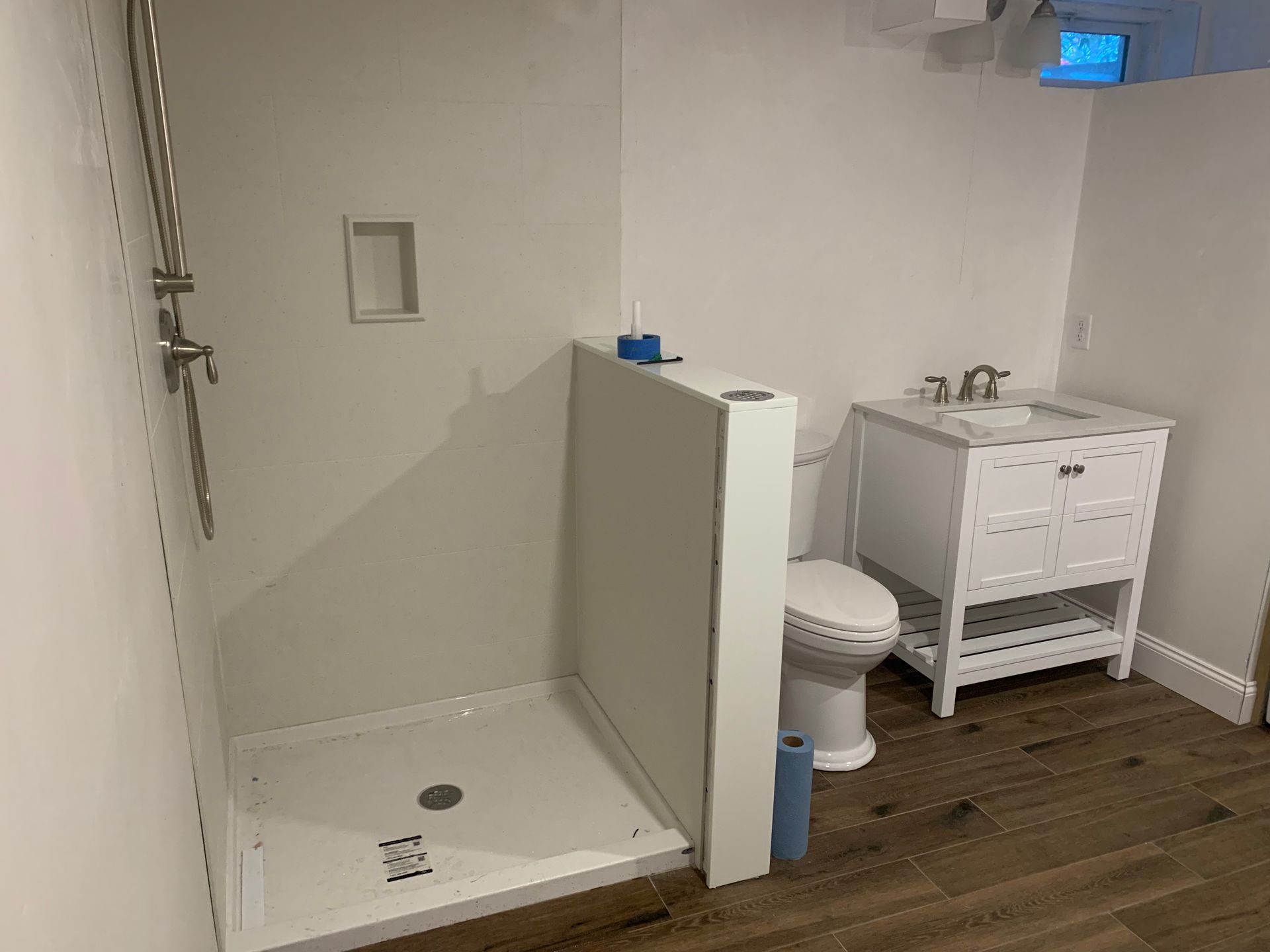 Bathroom with white shower stall, toilet, vanity, and wood-look floor.