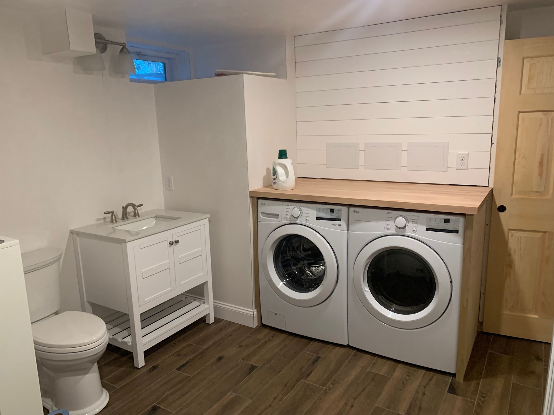 Laundry room with a washing machine, dryer, sink, toilet, and wooden door.