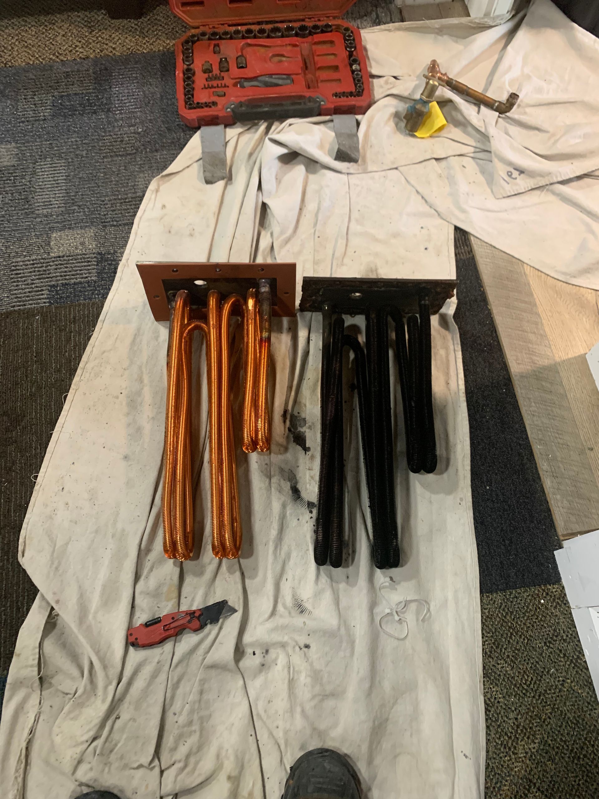 Two heat exchanger cores: copper (left), black (right) on a drop cloth with tools.