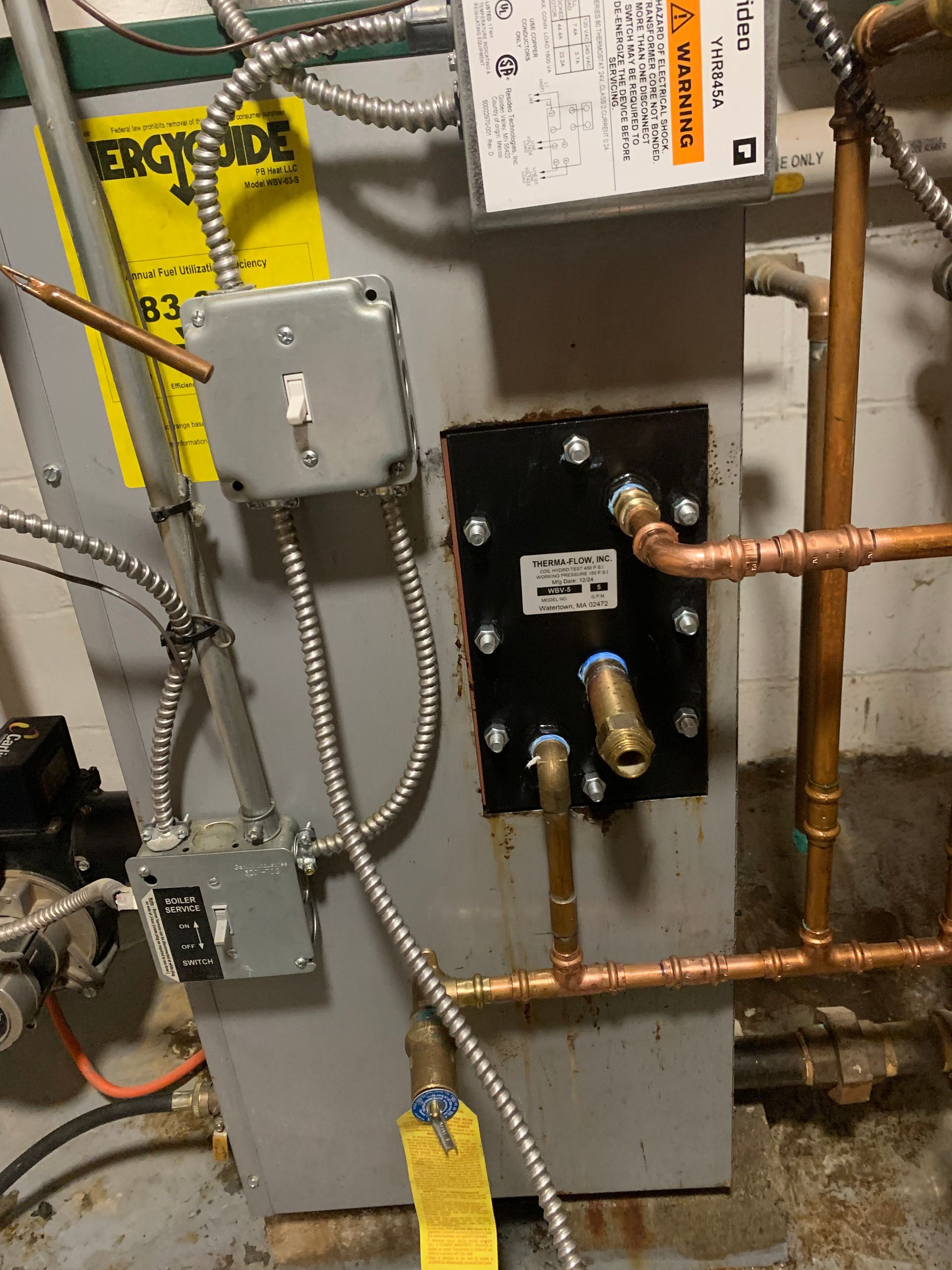 A close-up of a water heater with copper pipes, electrical boxes and wiring.