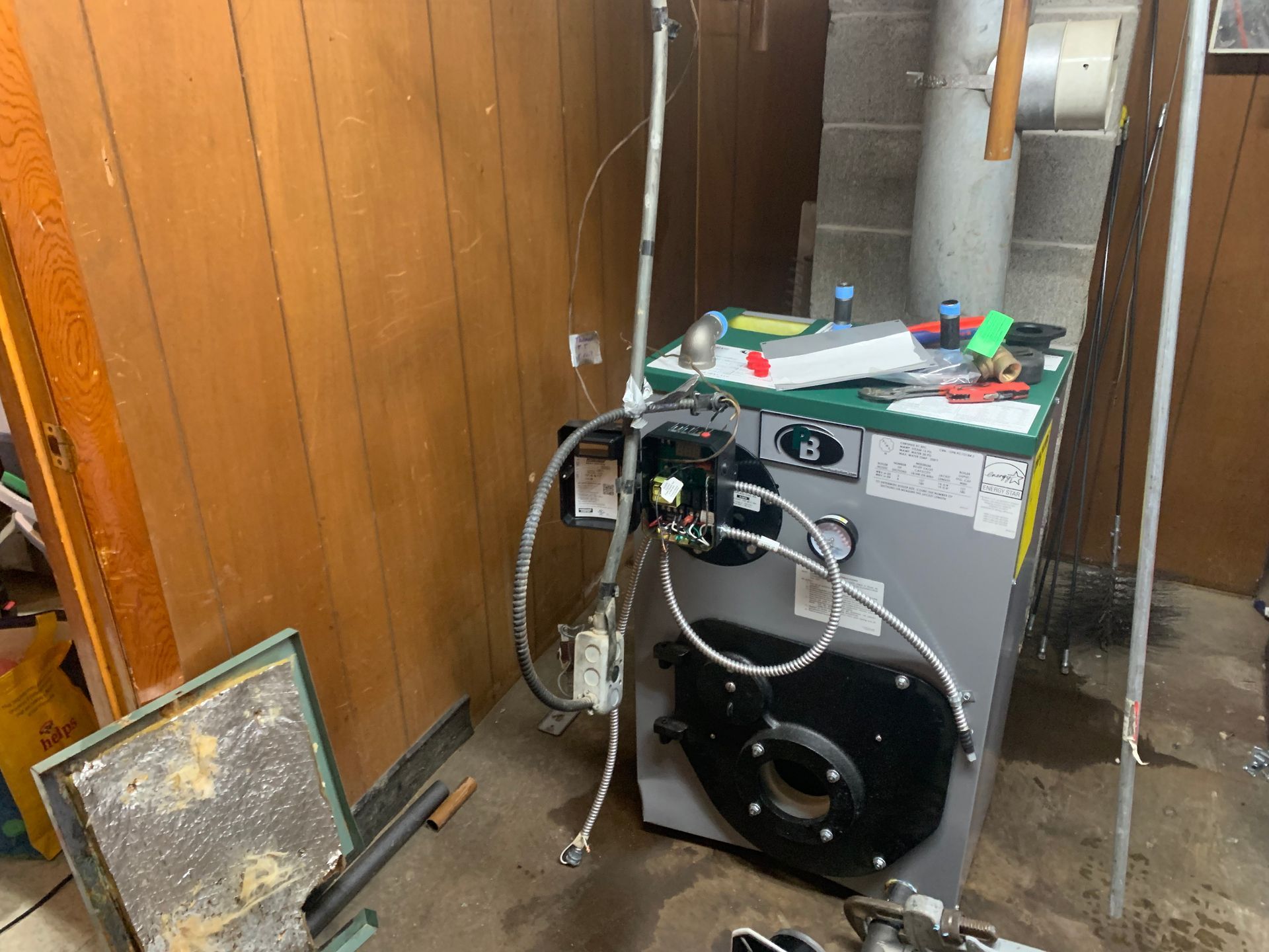 Oil-fired boiler in a basement setting, surrounded by piping and tools.