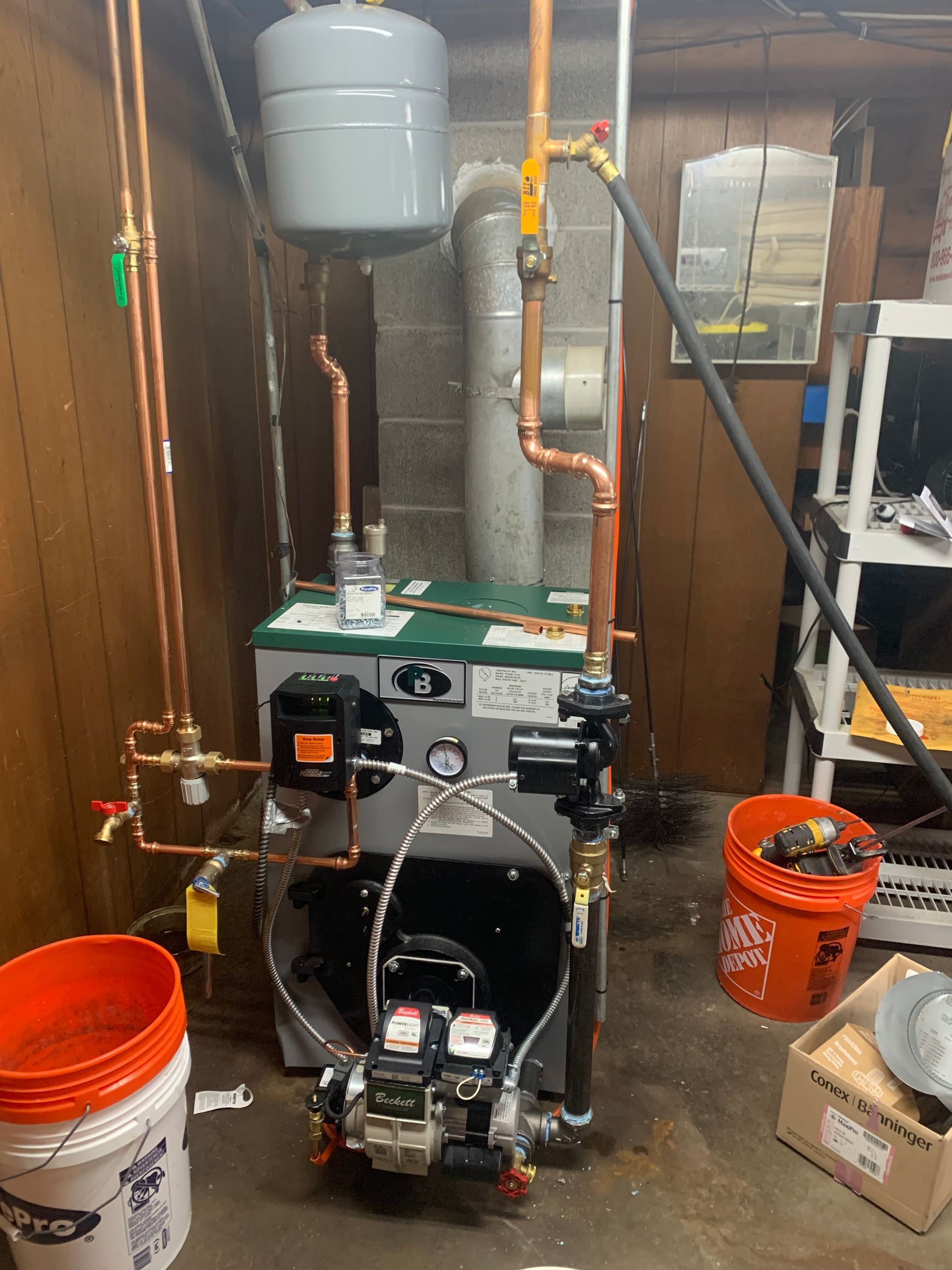 Oil-fired boiler system with copper pipes, expansion tank, and control panel in a utility room.