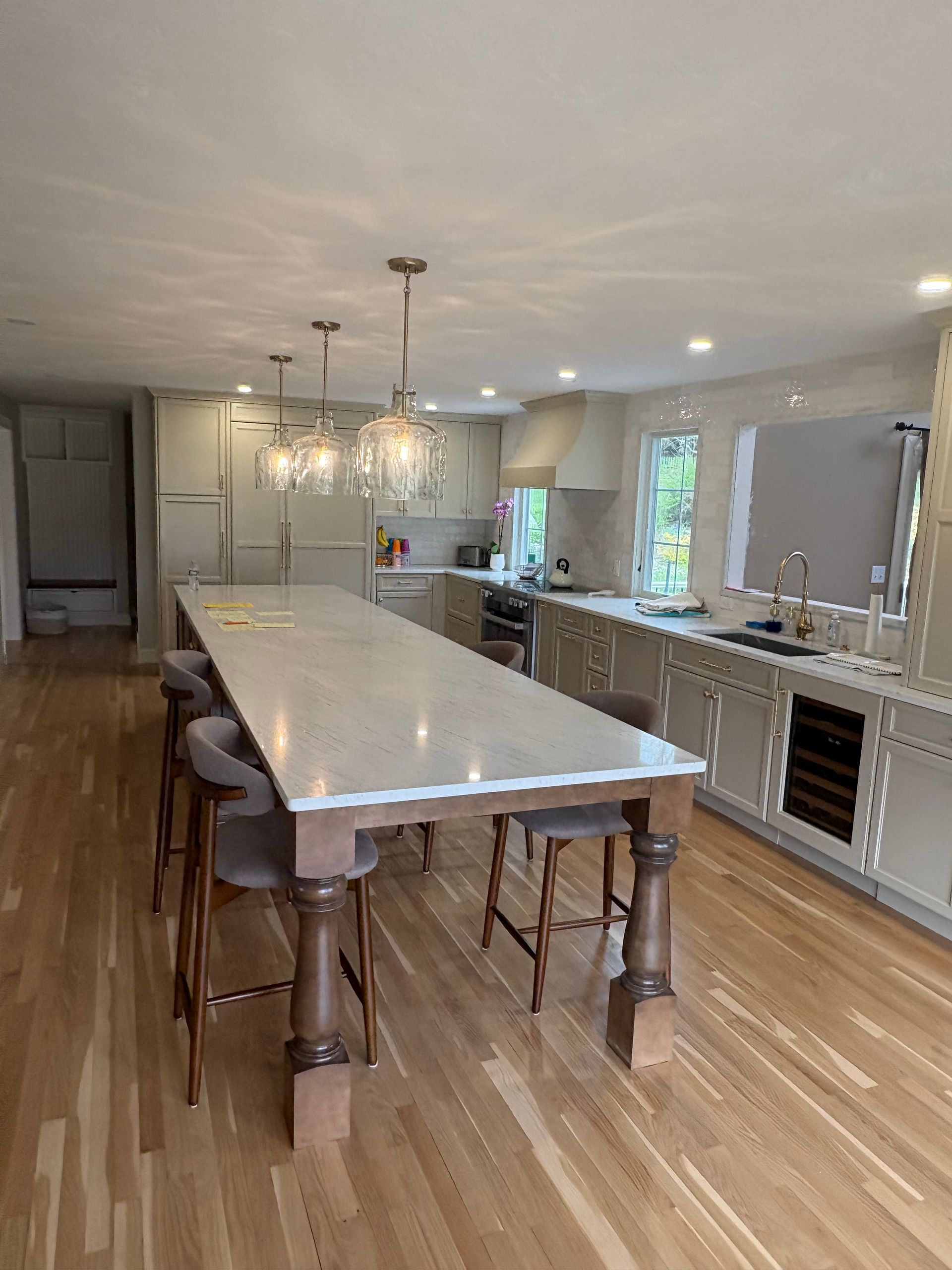 Bright modern kitchen with a long white island, wooden stools, pendant lights, and stainless appliances