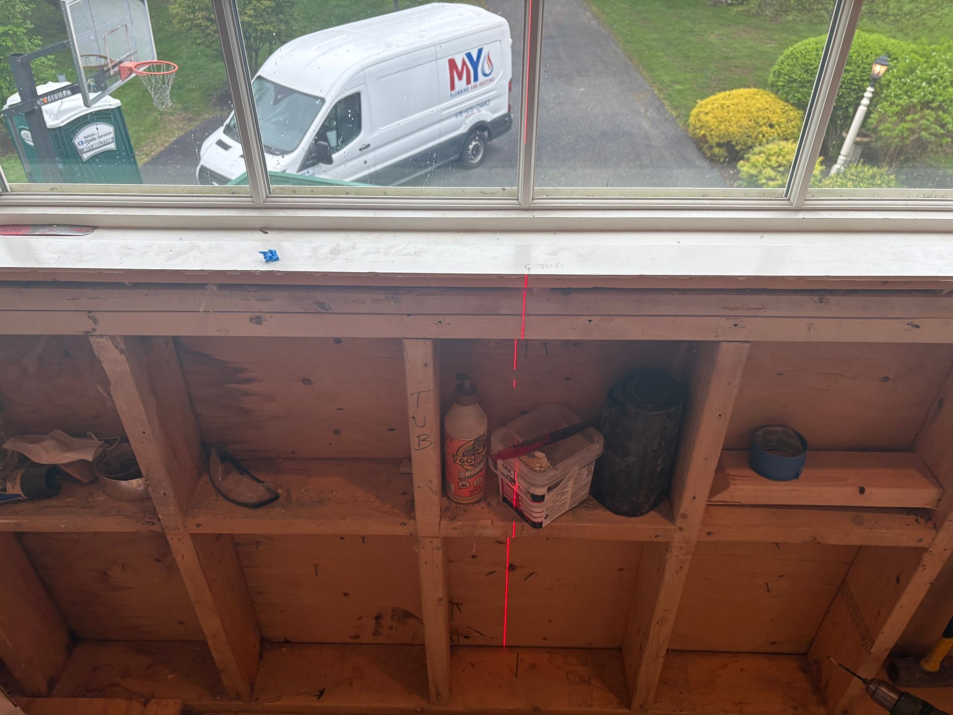 View from a window into a wooden storage structure. Red string hangs. A white van is visible outside.