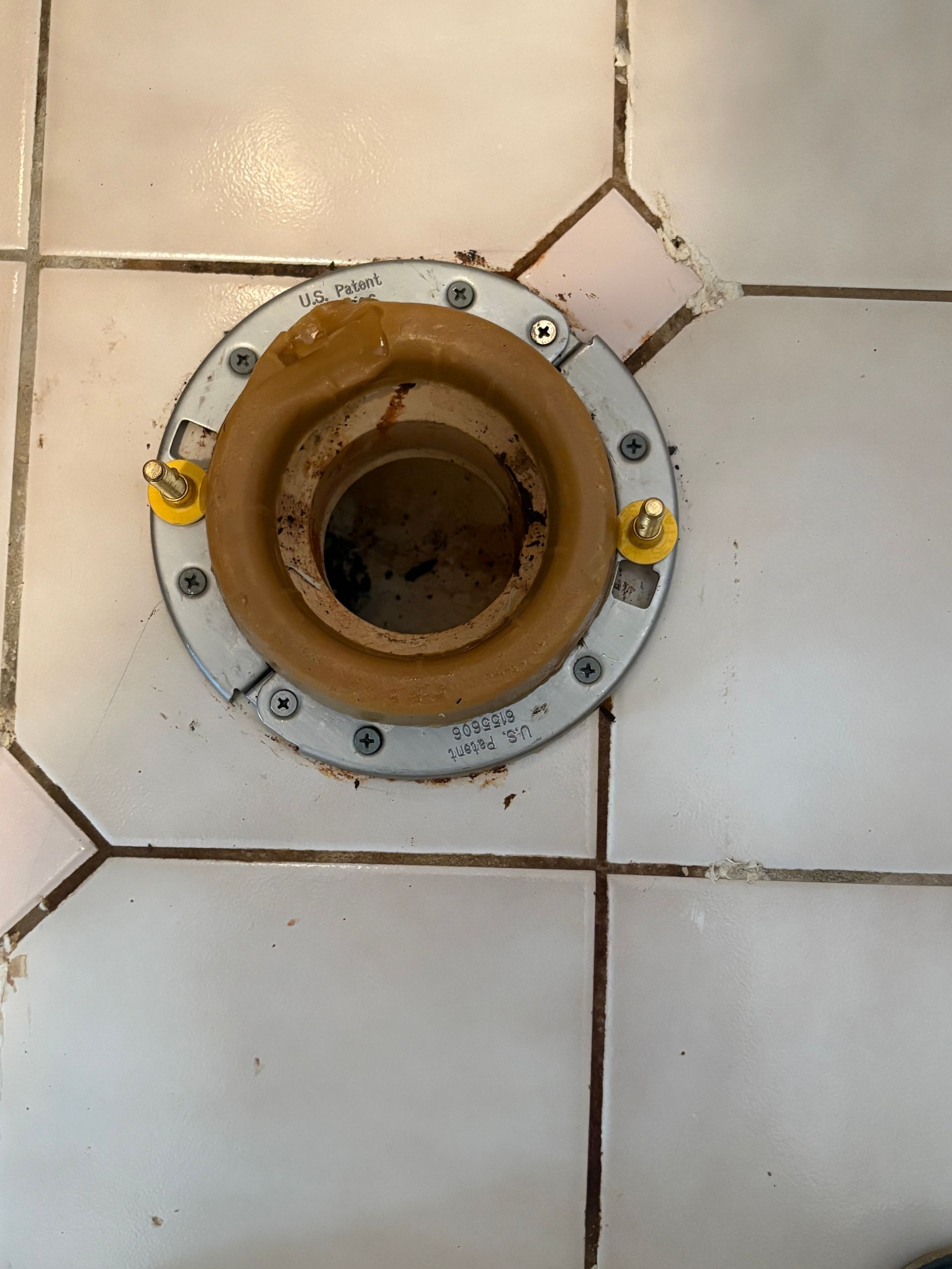 Open toilet drain flange in white tiled bathroom floor