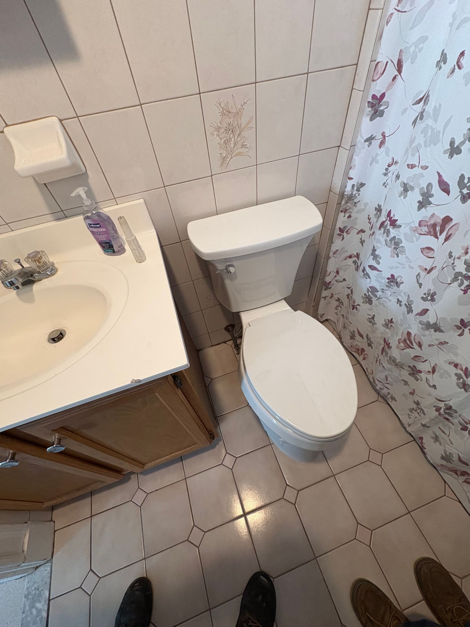 Small bathroom with toilet, sink, tiled floor, and floral shower curtain.