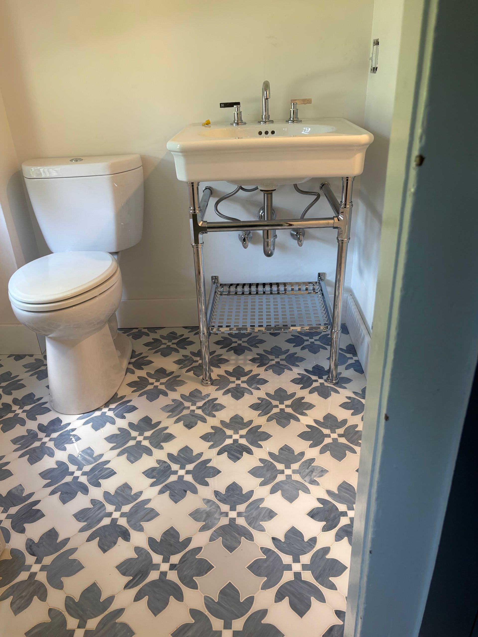 Small bathroom with toilet, pedestal sink, and blue patterned tile floor.