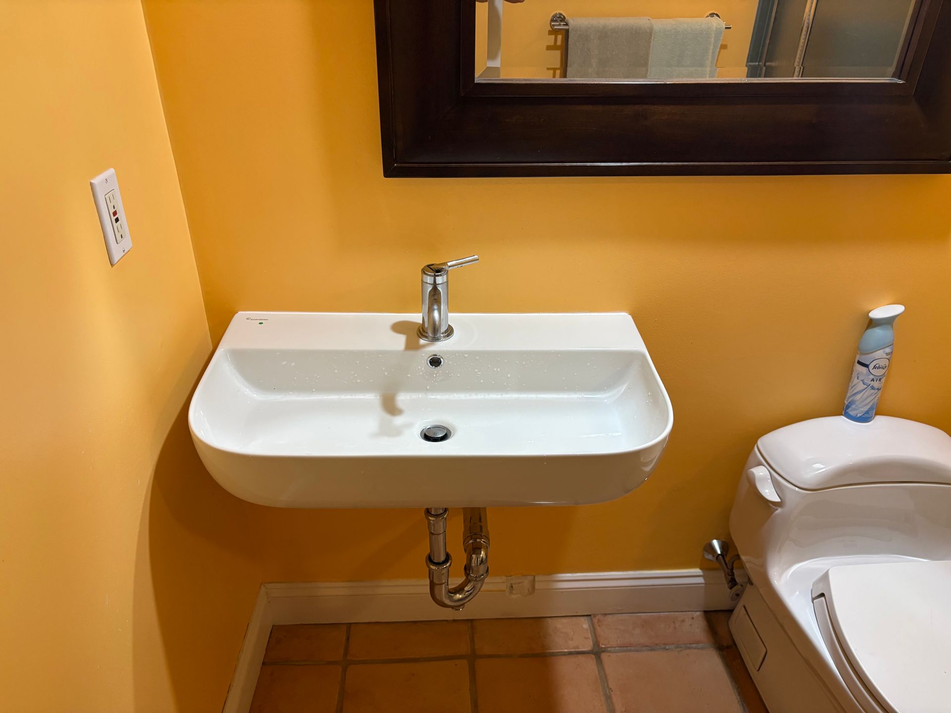 White sink and mirror on an orange bathroom wall, with a toilet visible on the right.
