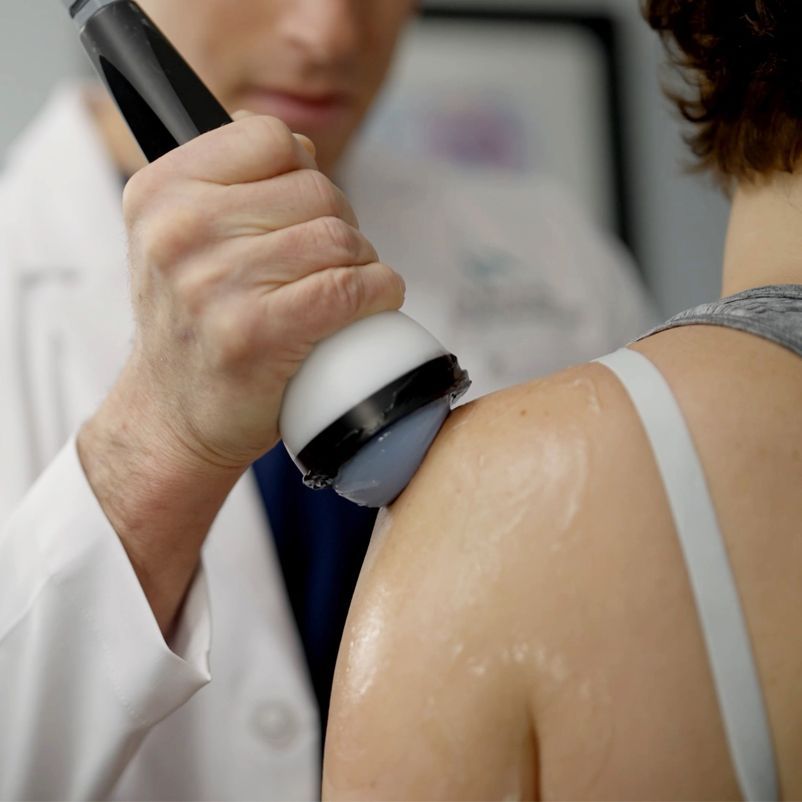 A man is using a device on a woman 's shoulder