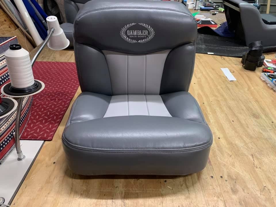 Gray and light gray boat seat with logo, placed on a wooden surface.