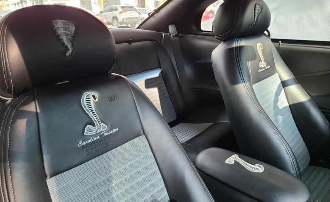 Interior of a black and gray Ford Mustang Cobra with Cobra emblems embroidered on the seats.