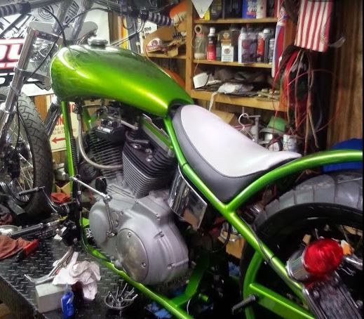 Green custom motorcycle in a cluttered garage with a white seat.