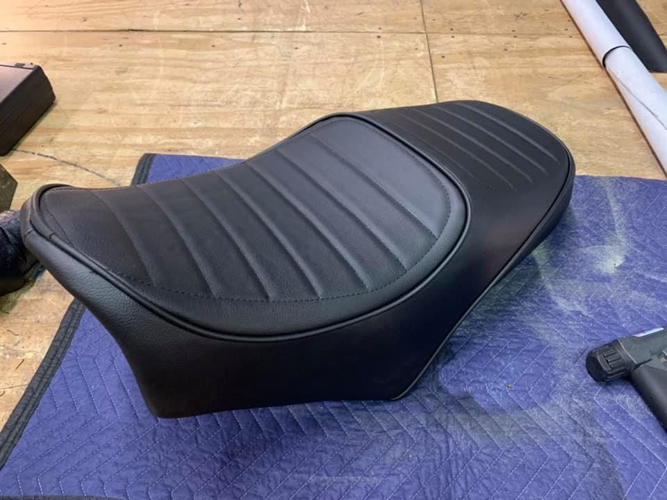 Black motorcycle seat with ribbed detailing, set on a blue mat, in a workshop.
