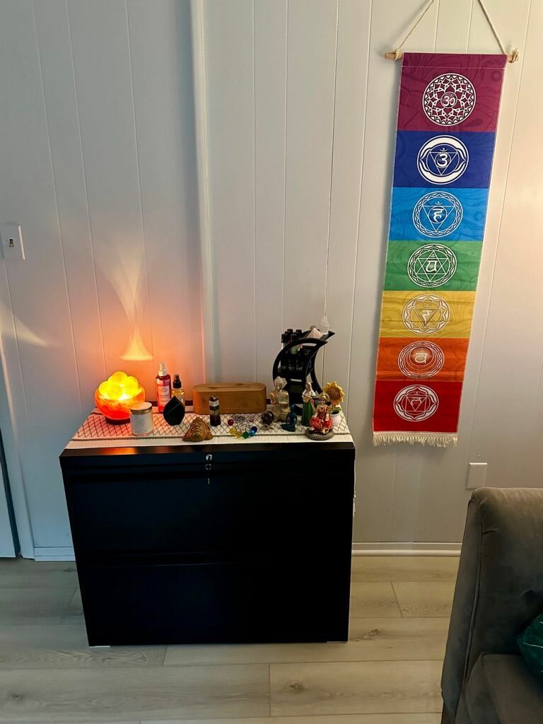 Woman meditating, seated in a chair, eyes closed, hands open. Light from a stained-glass lamp above.