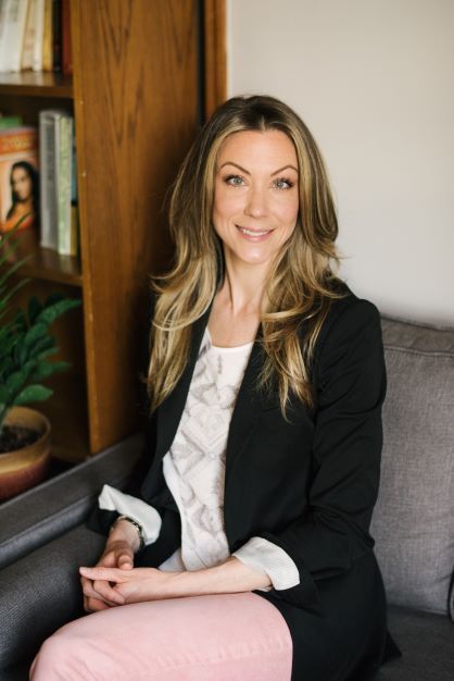 Woman with eyes closed, hand on chest, meditating in front of a green wall, wearing a light tank top.