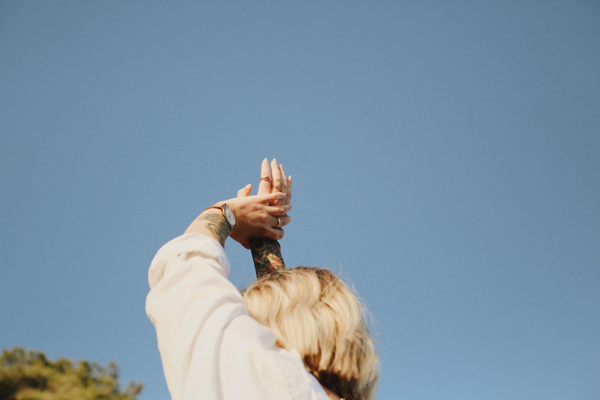 Person with blonde hair, raised arms holding a stick against a blue sky.