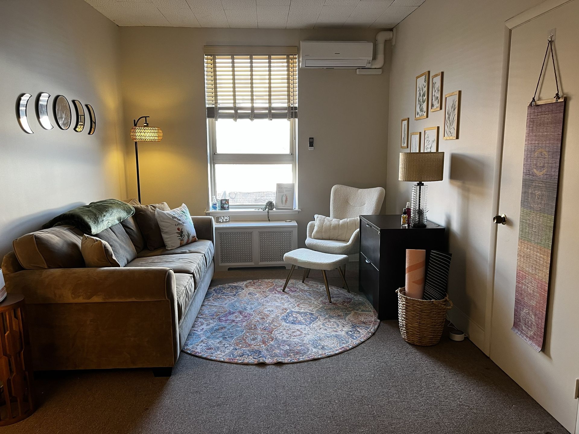 A cozy living room with a beige sofa, a patterned circular rug, a white armchair, and a small dark storage cabinet.