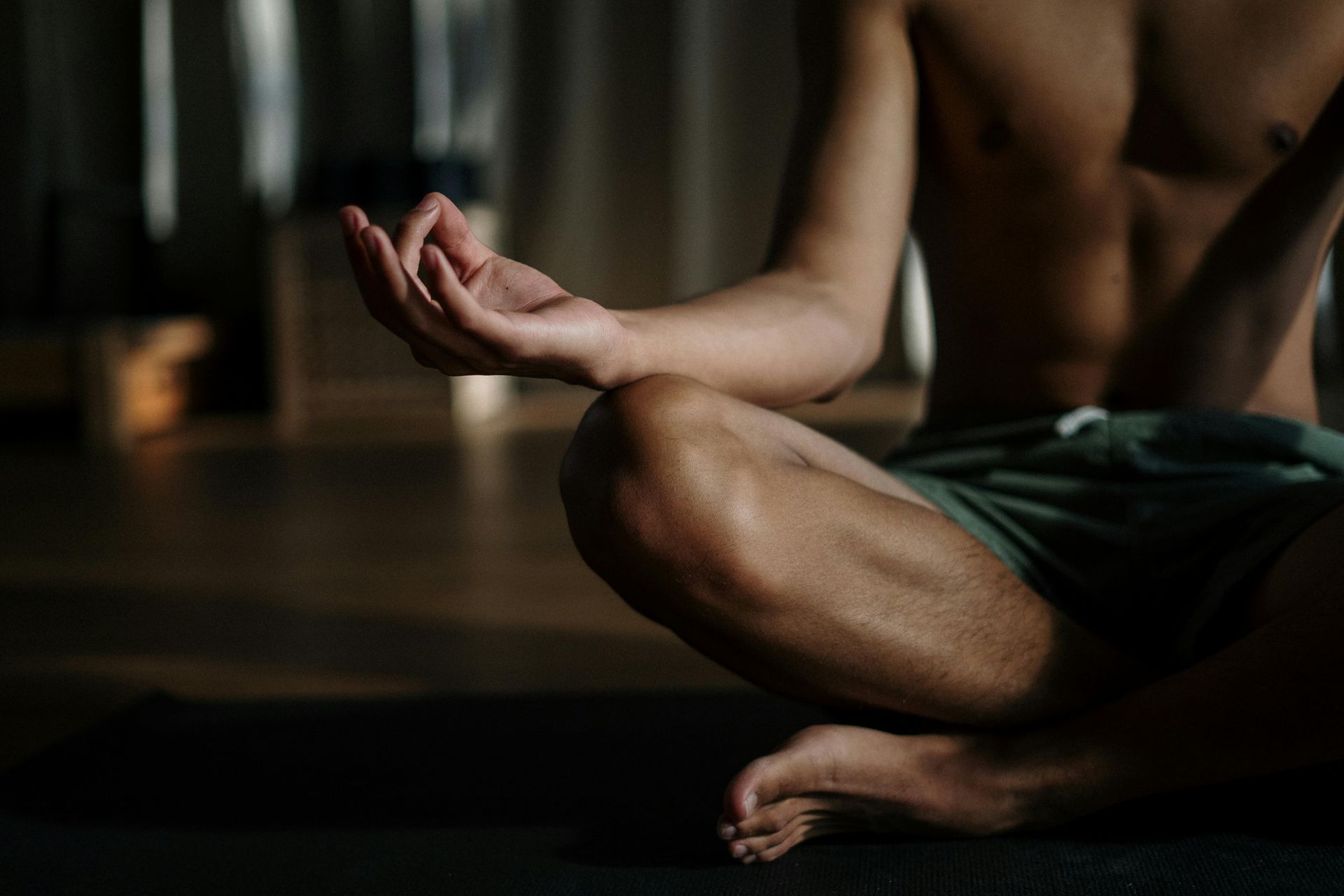 Person meditating, shirtless, in lotus position with hands in mudra, on a mat.