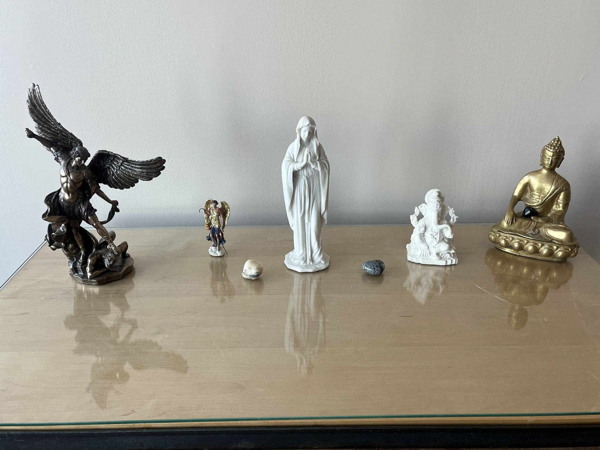 Five figurines and two stones arranged on a reflective glass table against a plain white wall.