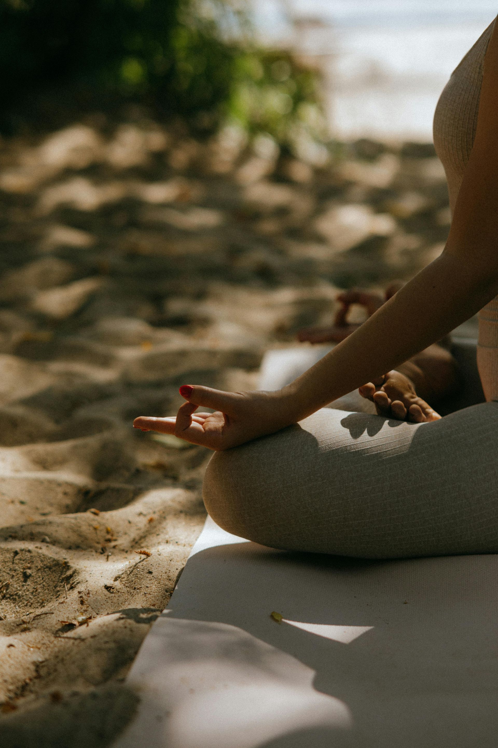 Person meditating on the beach, hand in mudra, sunlight.