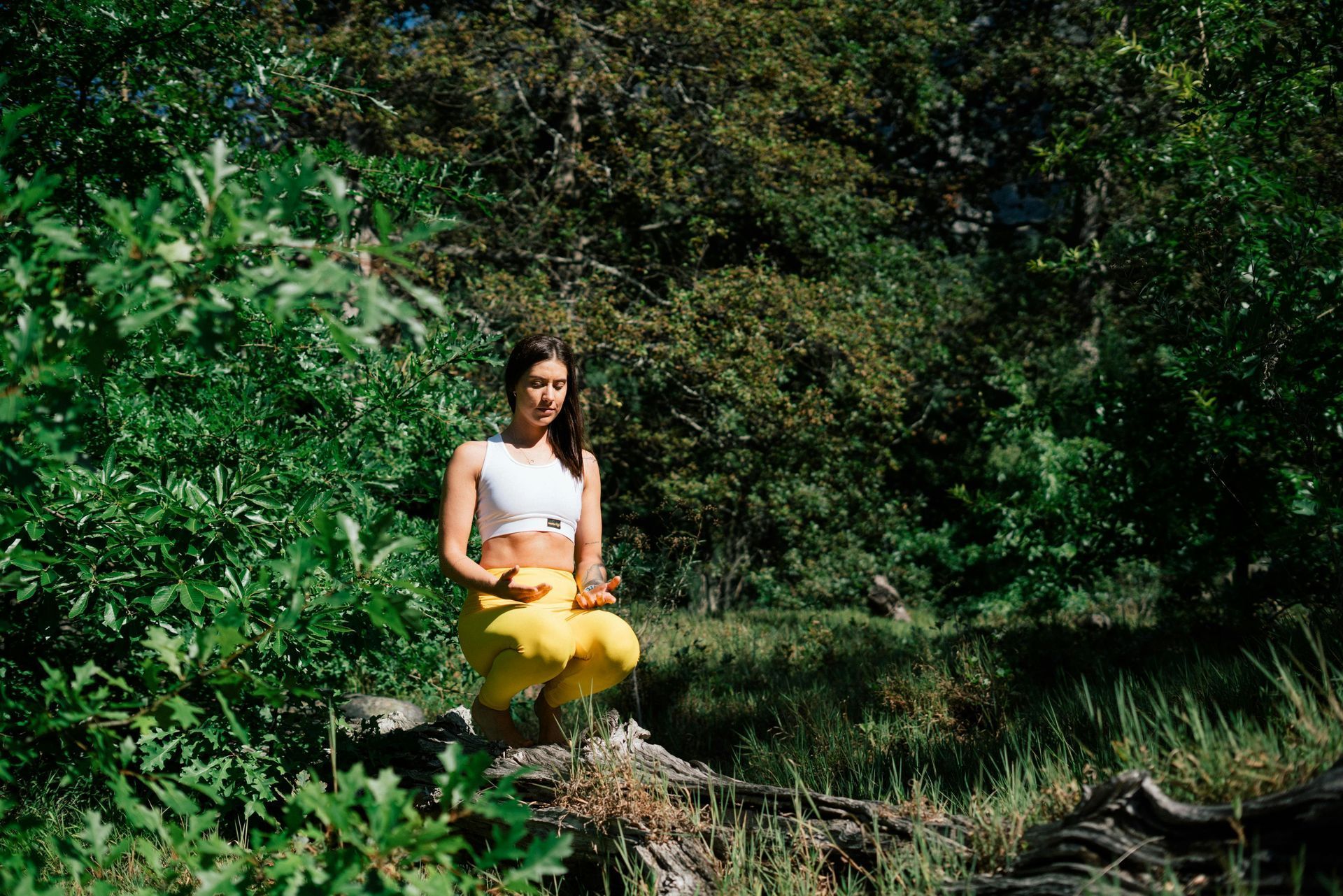 Woman in white top and yellow pants meditates outdoors.