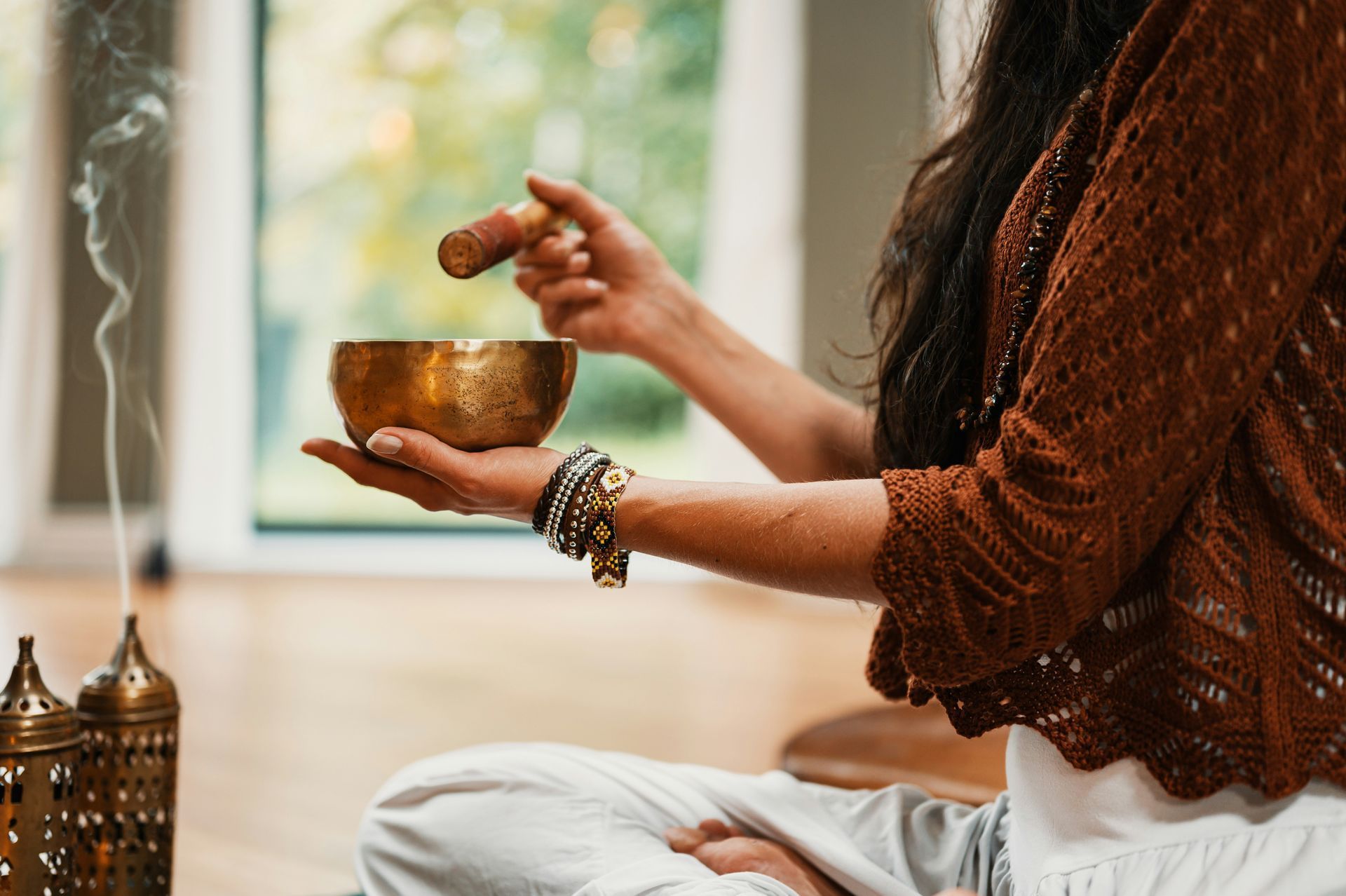 Person seated, playing a golden singing bowl, with incense burning nearby.