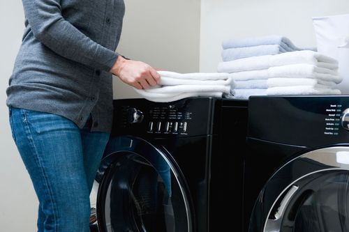 Person placing folded towels on top of a washing machine in a laundry room