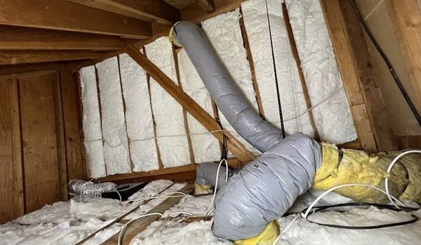 Attic with insulation and ductwork between wooden beams.