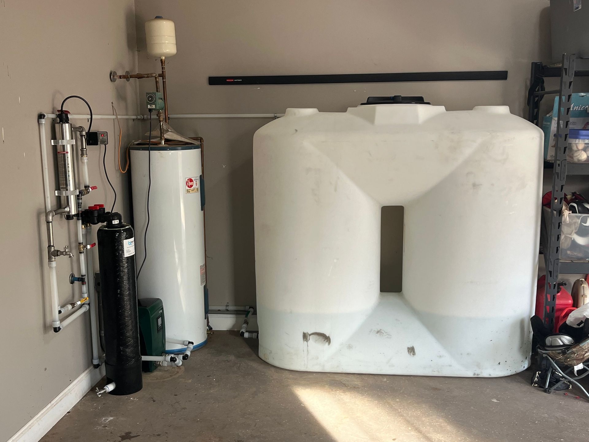 A large white tank is sitting next to a water heater in a garage.