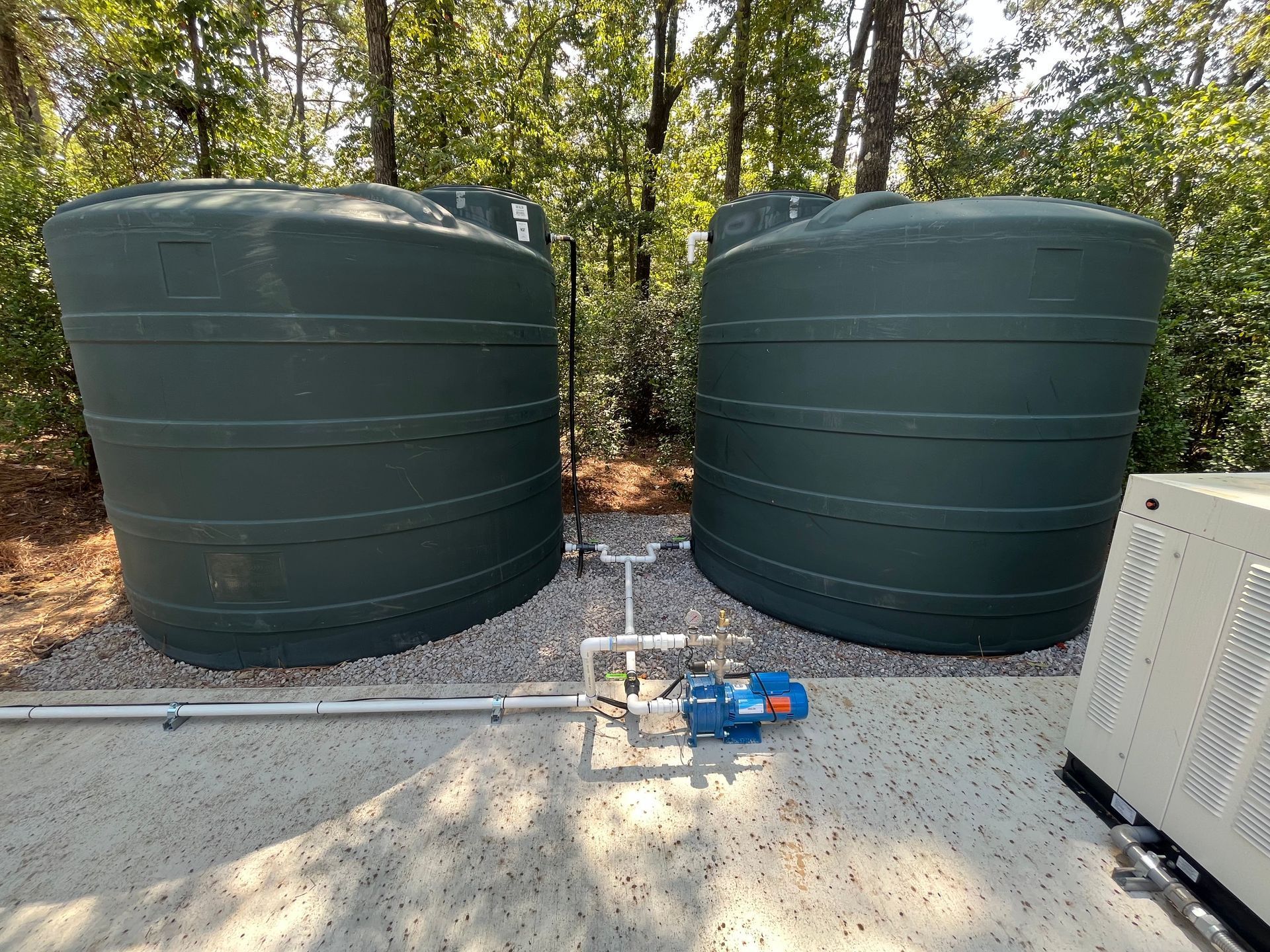 Two green water tanks are sitting next to each other on a gravel area.