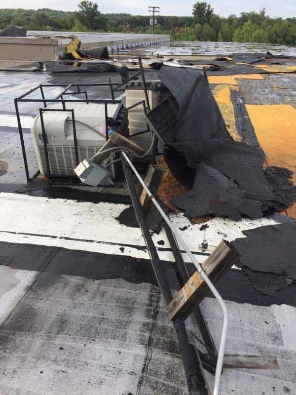 Damaged rooftop: air conditioning unit, torn roofing, and debris on a flat roof.