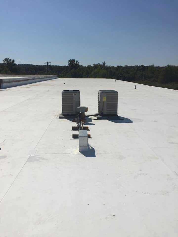 White commercial rooftop with two air conditioning units under a clear blue sky.
