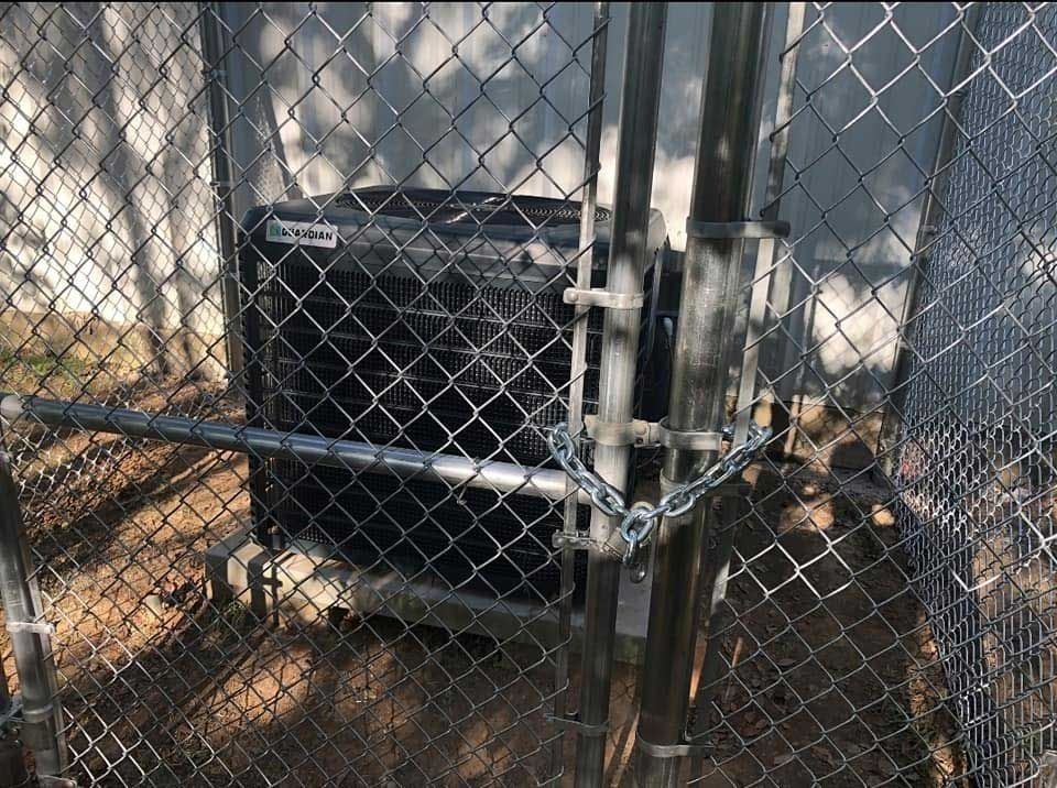 Air conditioning unit secured inside a chain-link fence enclosure, locked with a chain.