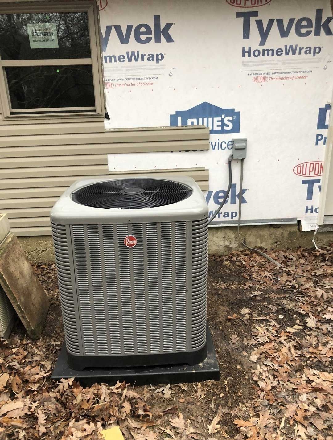 Air conditioner unit outside a house, with Tyvek wrap visible.