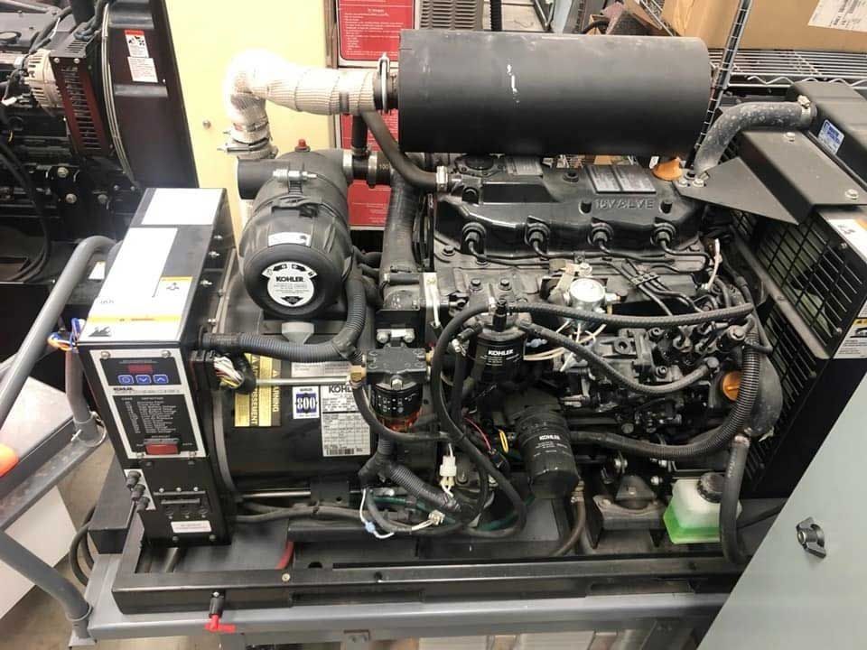 Diesel generator, black and grey, on a metal frame. Engine with exhaust and control panel.