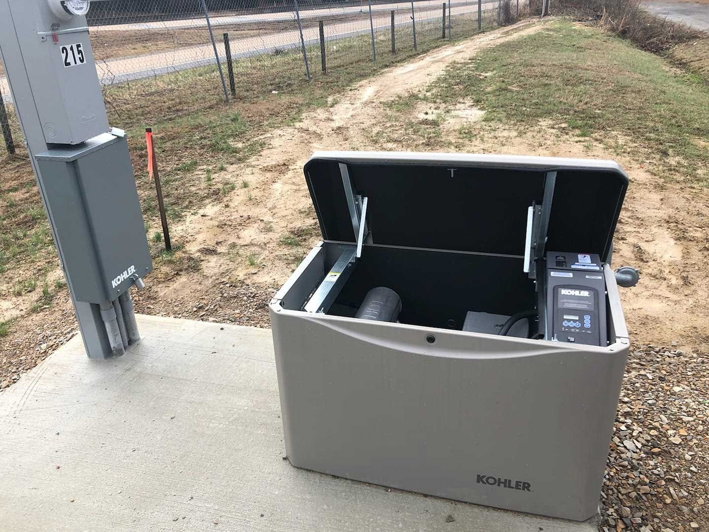 Gray open electrical box on a concrete pad, next to a utility pole, outdoors.