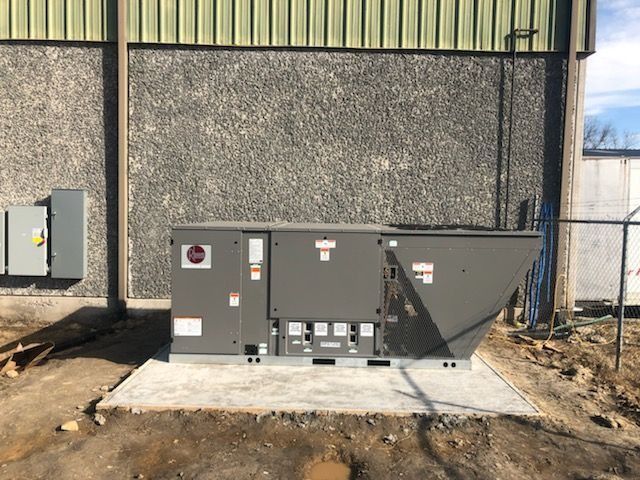 Gray HVAC unit on a concrete pad next to a building. Electrical box on the left.