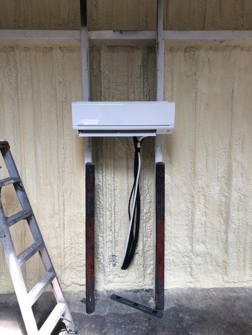 Mini-split AC unit mounted on a steel frame against a foam-insulated wall; ladder on left.
