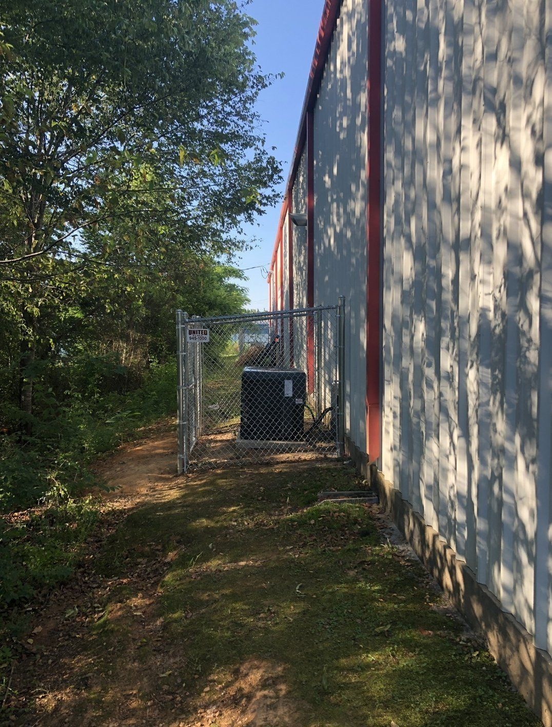 Chain-link fence surrounds AC unit next to industrial building.