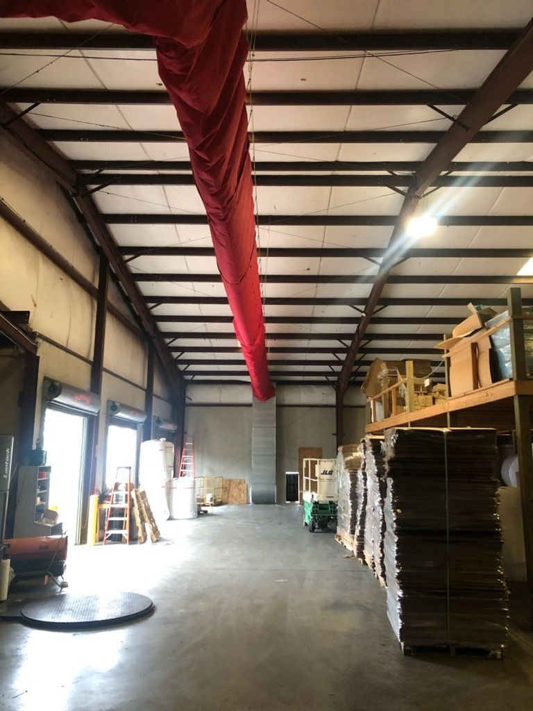 Warehouse interior with red fabric duct, metal beams, concrete floor, and stored materials.