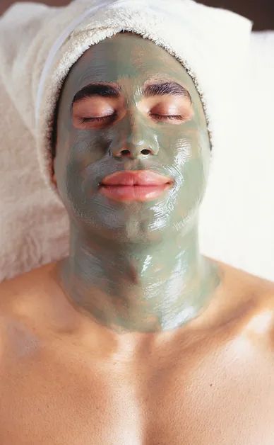 A man is laying on a bed with a clay mask on his face.