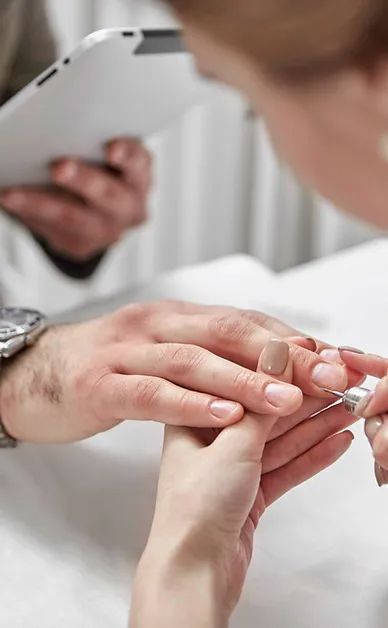 A woman is getting her nails done by a man while a man looks at his phone.