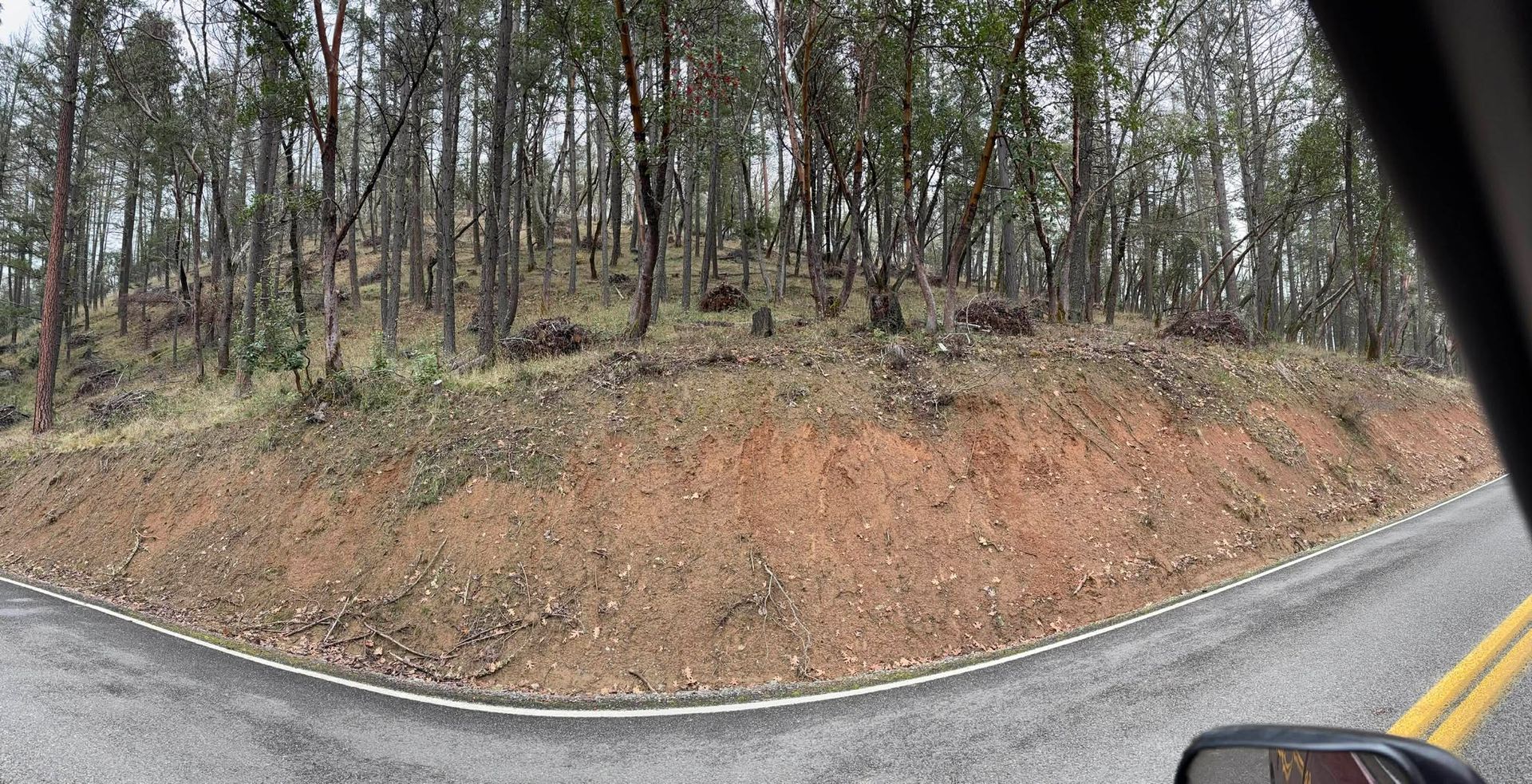Intersection of two roads with a wooded hillside in the background. Brown earth and trees.