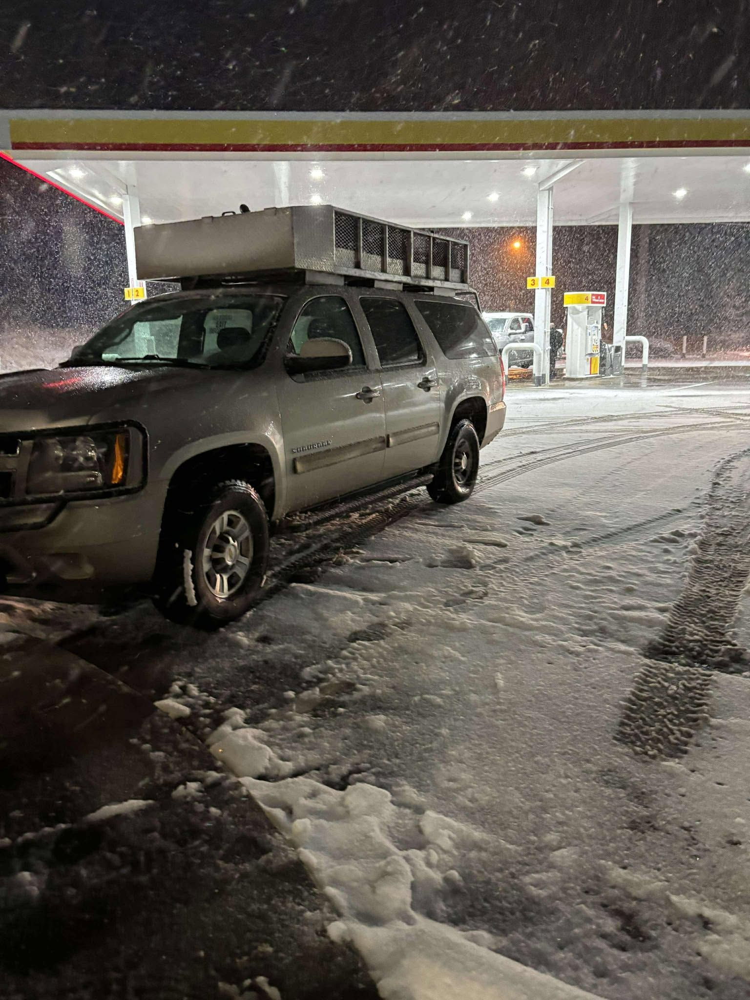 SUV with boxes on top, at a gas station, in snowy conditions.