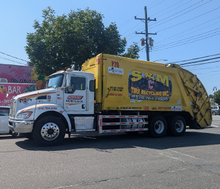 A yellow garbage truck is parked on the side of the road.